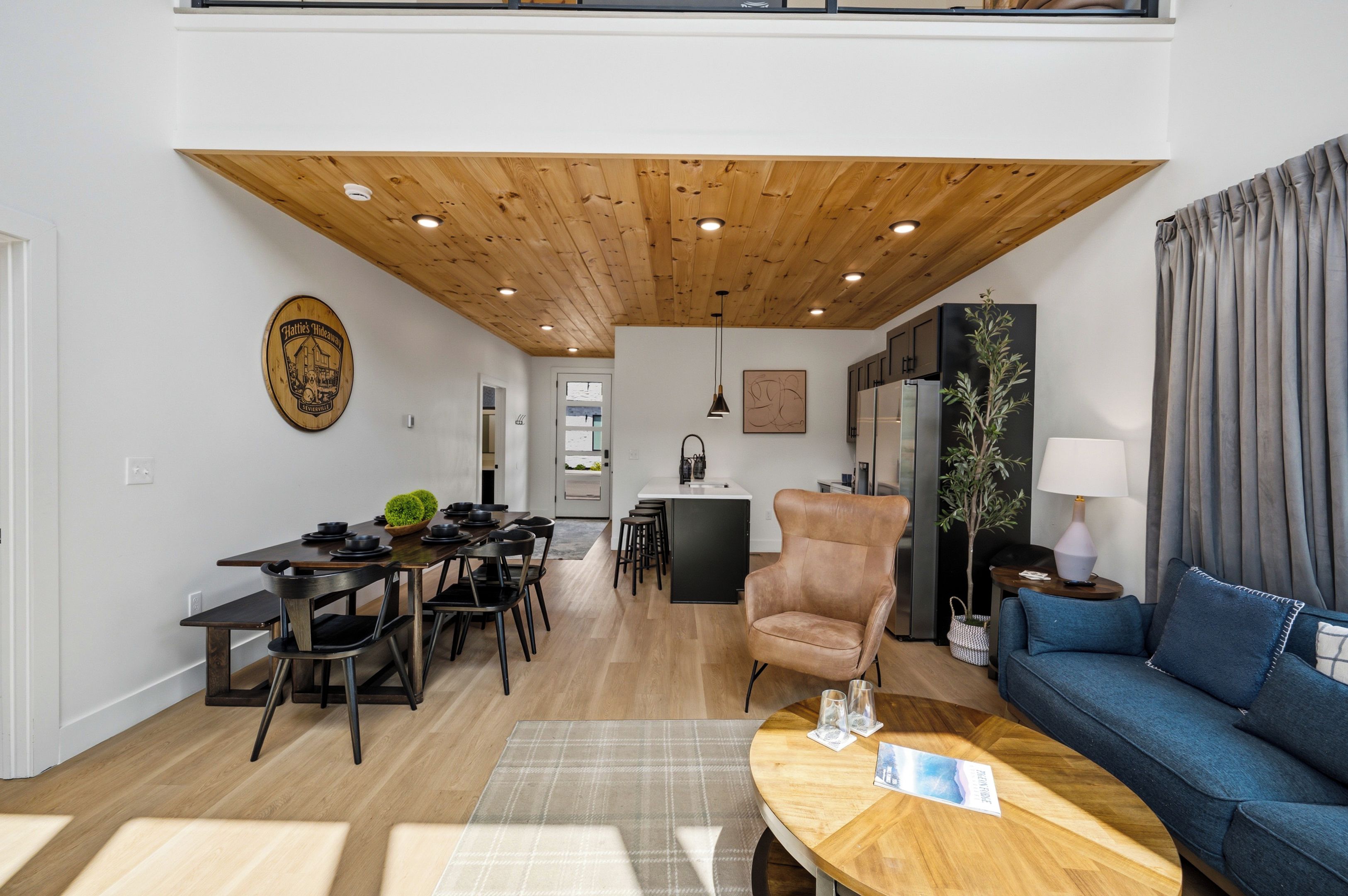A modern living room with a dining area, a wooden ceiling, and a view of the kitchen.