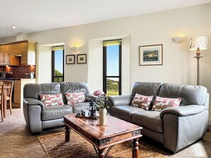 A living room with two grey leather sofas, a wooden coffee table, and a kitchen in the background. - Beehive Cottage, Culbone (Porlock)