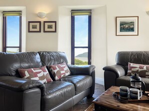 A living room with a leather sofa, two framed pictures, and a coffee table with mugs. - Beehive Cottage, Culbone (Porlock)