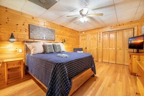 Een kamer met houten lambrisering, een bed, nachtkastjes, een plafondventilator en een televisie.