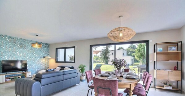 Een moderne woonkamer met een bank, een eettafel, stoelen, een televisie en een groot raam.