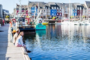 Eine Steg mit Menschen am Wasser, Boote im Hintergrund und farbenfrohe Gebäude entlang der Uferlinie.