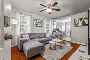 A modern living room with a grey sectional sofa, a ceiling fan, and a small round table. - East Hill Manor Large Double Apartment Villa (Pensacola)