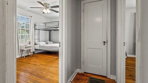 A room with a bunk bed, a desk, a chair, a ceiling fan, and a door. - East Hill Manor Large Double Apartment Villa (Pensacola)