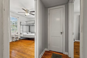 A room with a bunk bed, a desk, a chair, a ceiling fan, and a door. - East Hill Manor Large Double Apartment Villa (Pensacola)