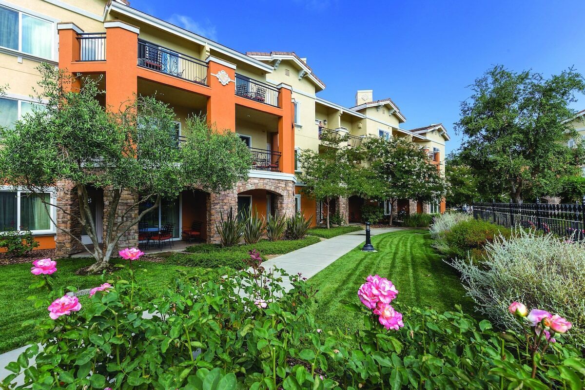 A multi-story residential building with balconies, a well-maintained lawn, and flowering plants.