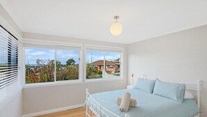 Um quarto com cama, paredes brancas, janela com vista e luminária no teto.