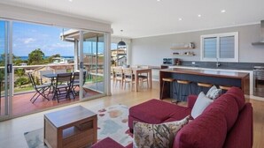 Sala de estar moderna com uma ampla porta de vidro deslizante que dá para uma varanda, área de cozinha com balcão e um espaço de estar com sofá vermelho.