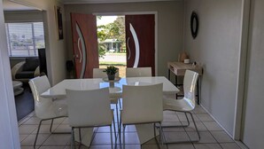 Una zona de menjador amb una taula i cadires blanques, una petita planta en test i vistes cap a l'exterior.