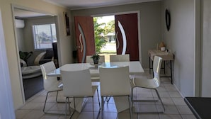 Zona de menjador amb una taula rodona i sis cadires, una taula auxiliar amb un vas i una porta que dona a l'exterior.
