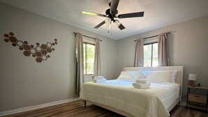 Ein Schlafzimmer mit Bett, Deckenventilator, Holzboden und einem Fenster mit Vorhängen.