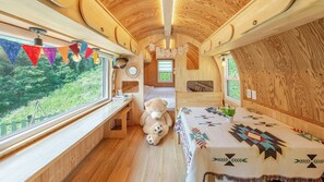 Un interior acogedor con techo de madera, una cama con manta estampada, un osito de peluche y una ventana con vistas a follaje.