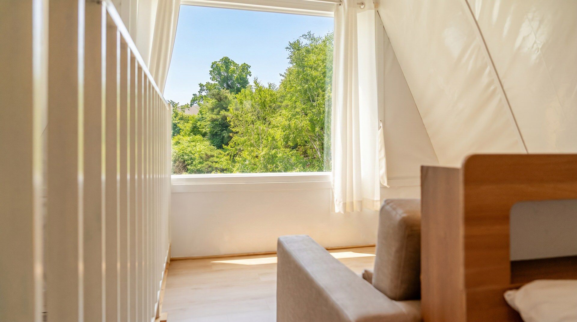 Quarto com janela dando para uma floresta, cama e cabeceira de madeira.