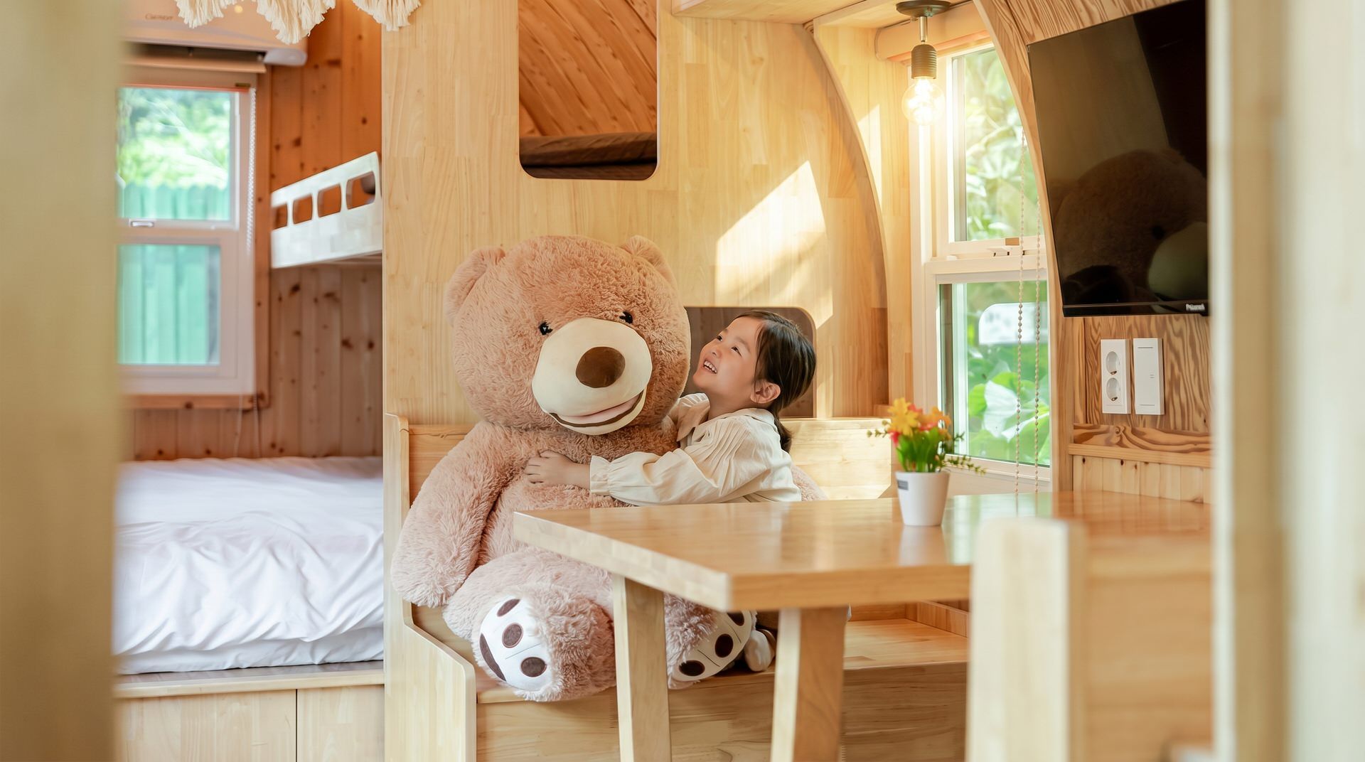 Uma cabana de madeira acolhedora com beliches, um urso de pelúcia grande e uma área de refeições.