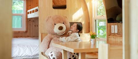 A cozy wooden cabin with bunk beds, a large teddy bear, and a dining area.