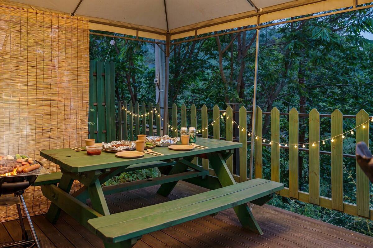 An outdoor dining area with a wooden table and benches, surrounded by a wooden fence and string lights.