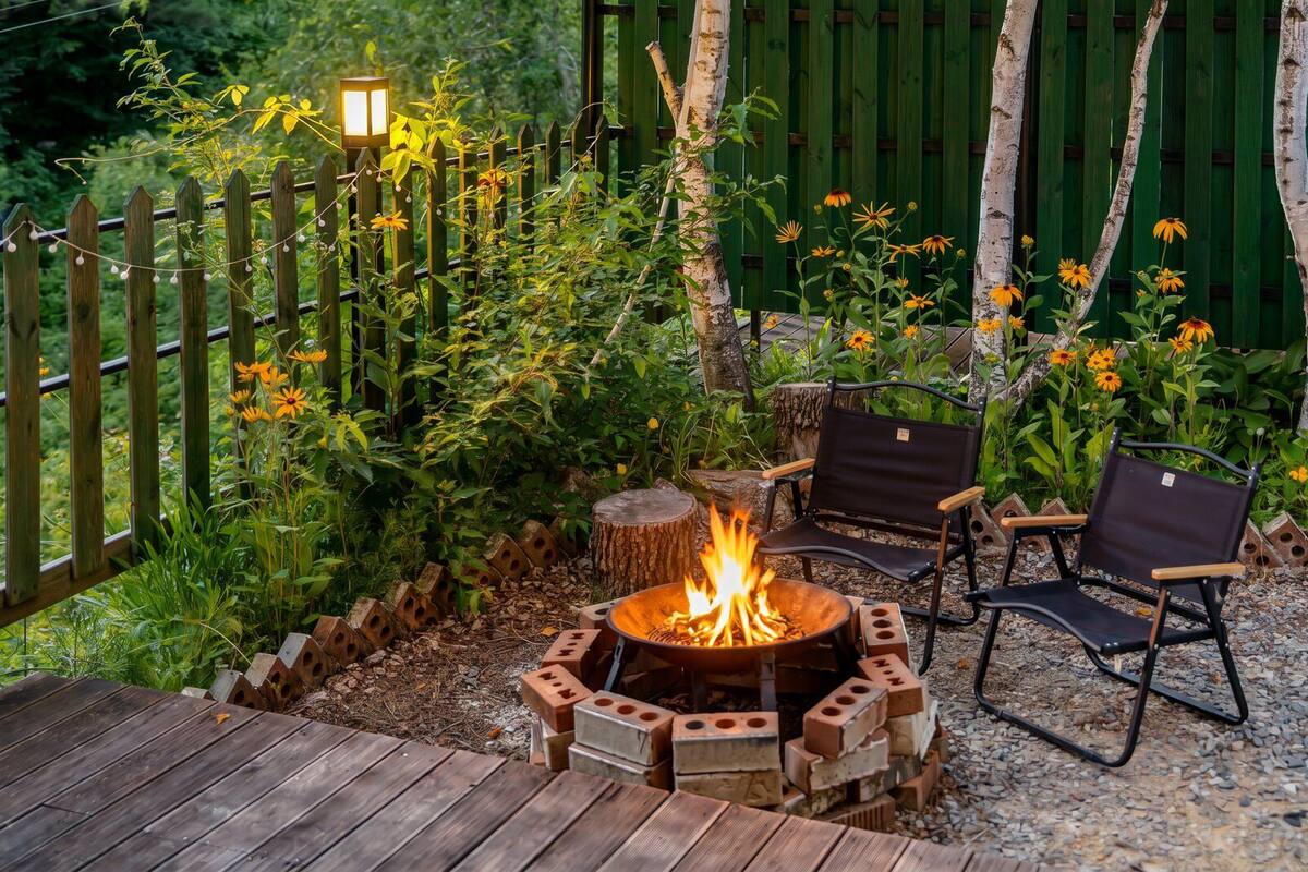 A fire pit surrounded by brick seating, a wooden deck, and a wooden fence with a lantern post.