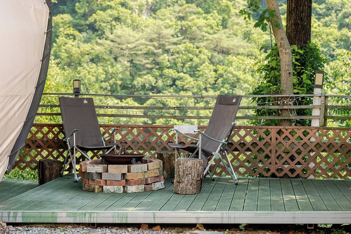 A deck with two chairs and a fire pit, surrounded by a wooden fence and a tent.