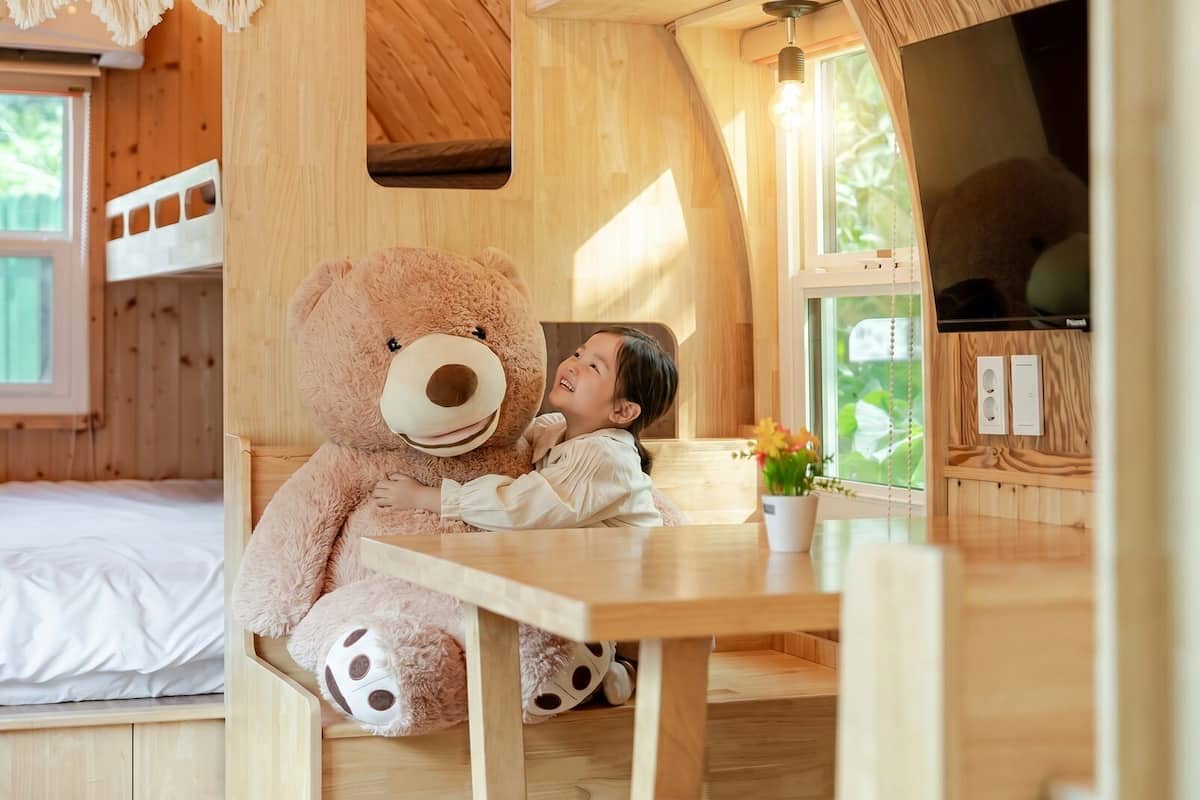 A cozy wooden cabin with bunk beds, a large teddy bear, and a dining area.
