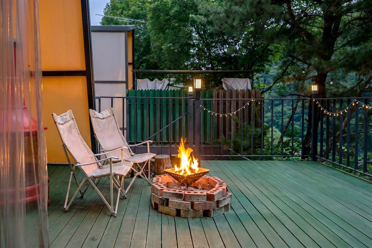 A deck with a fire pit, two chairs, and a view of trees.
