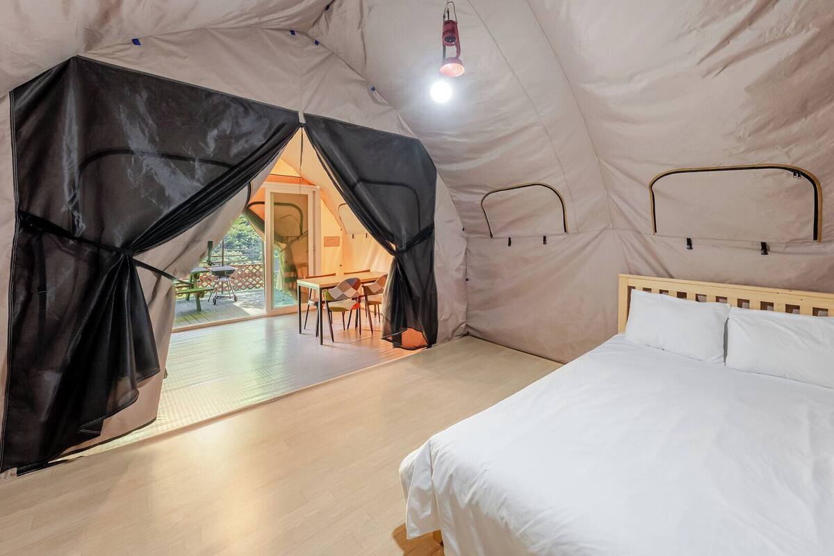 A tent with a bed, a table, chairs, and a hanging light fixture.