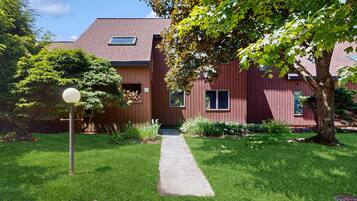 A red building with a paved pathway leading to the entrance, surrounded by greenery and a tree.
