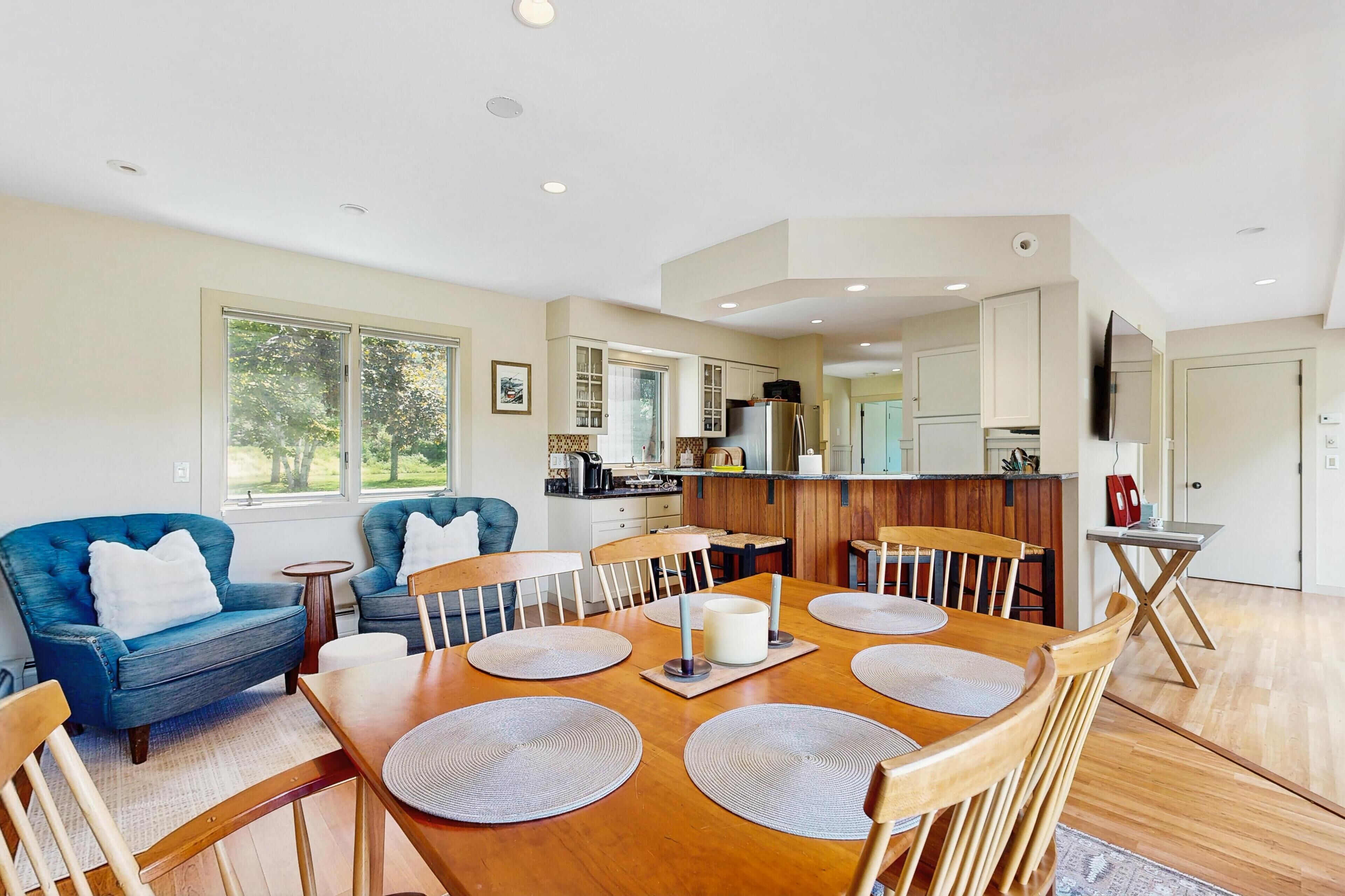 A dining area with a wooden table, blue sofas, and a kitchen in the background.
