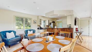 A dining area with a wooden table, blue sofas, and a kitchen in the background.