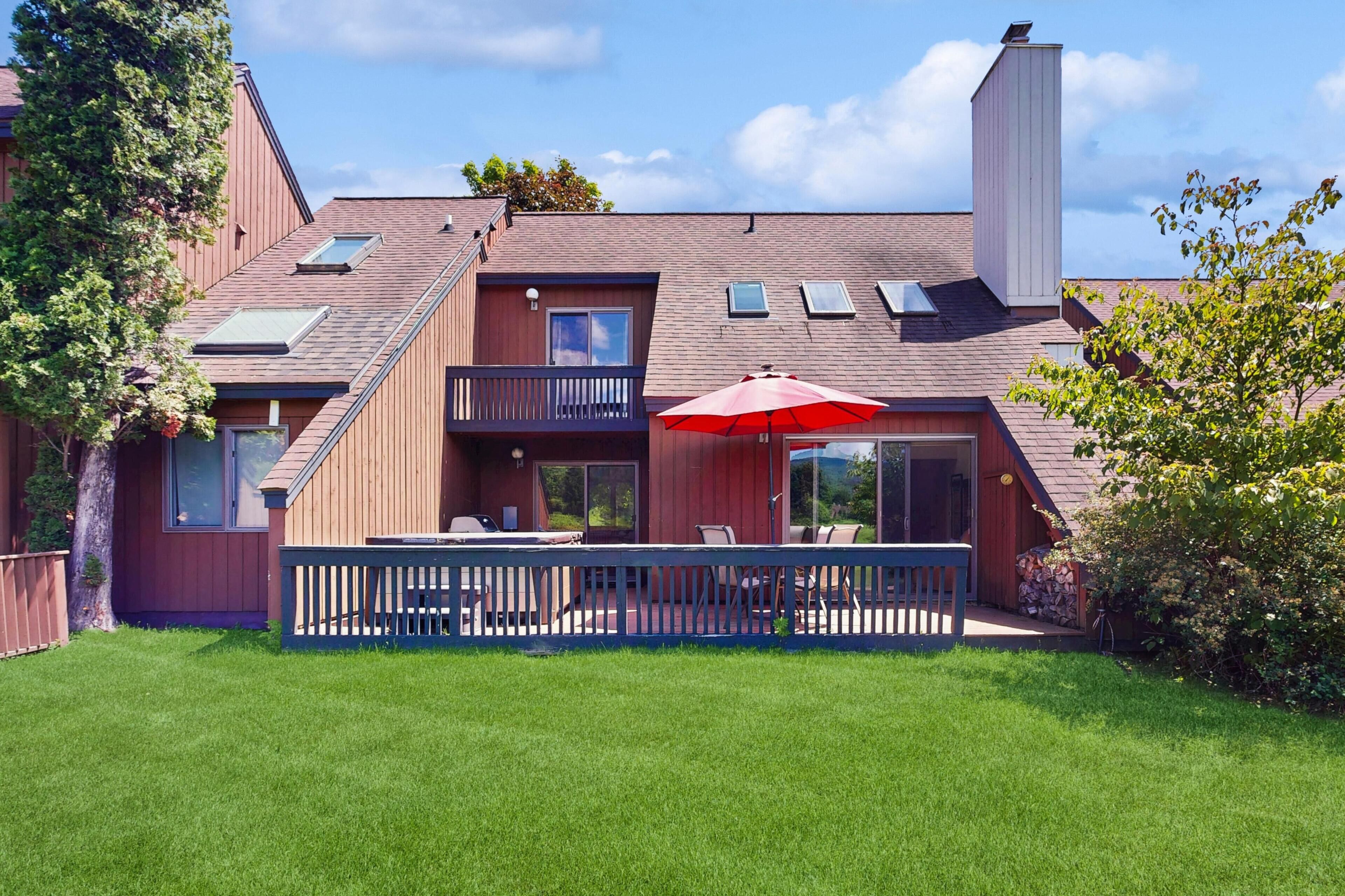A two-story house with a balcony, a red umbrella, and a well-maintained lawn.