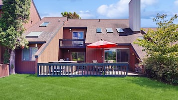 A two-story house with a balcony, a red umbrella, and a well-maintained lawn.