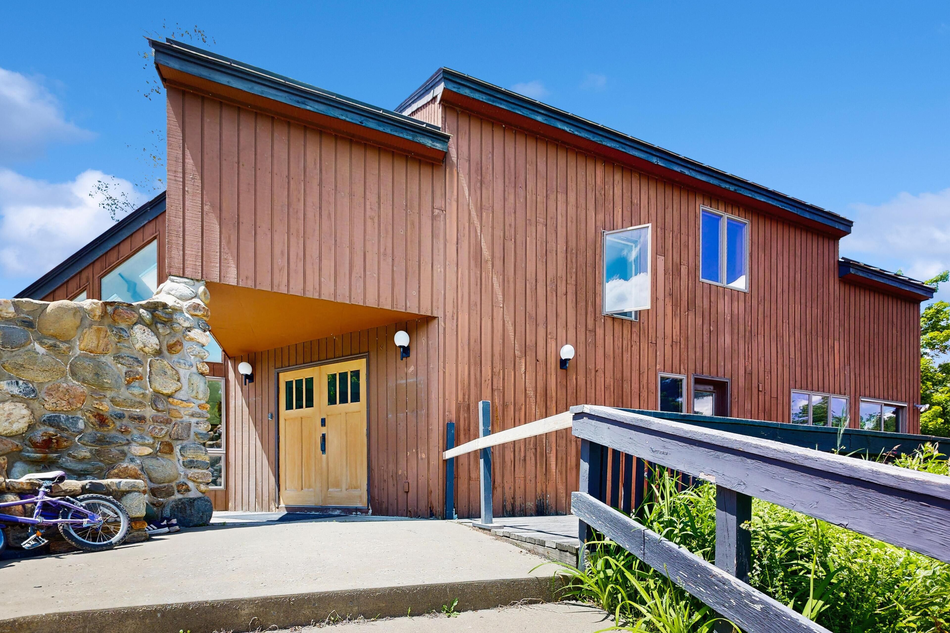 A wooden building with a stone wall entrance, a wooden door, and a ramp leading to the entrance.