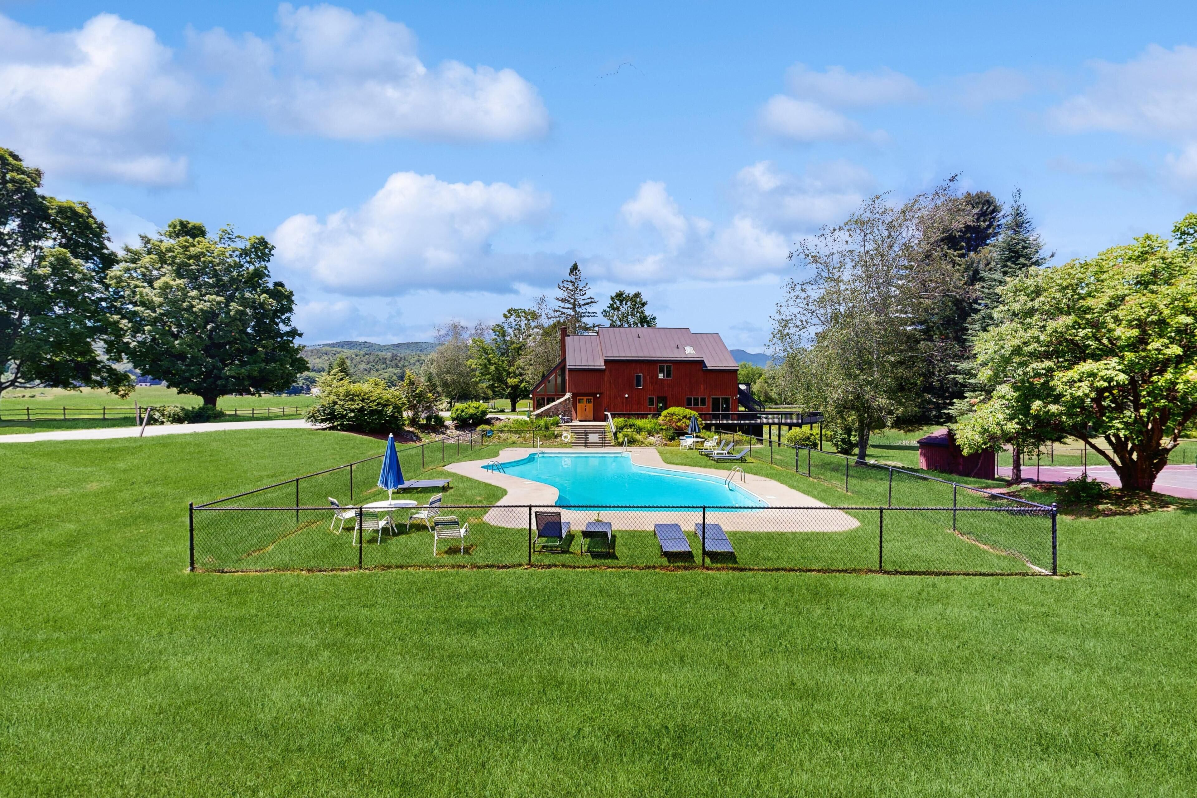 Ein Garten mit Zaun, Swimmingpool, Liegestühlen und einem roten Gebäude.