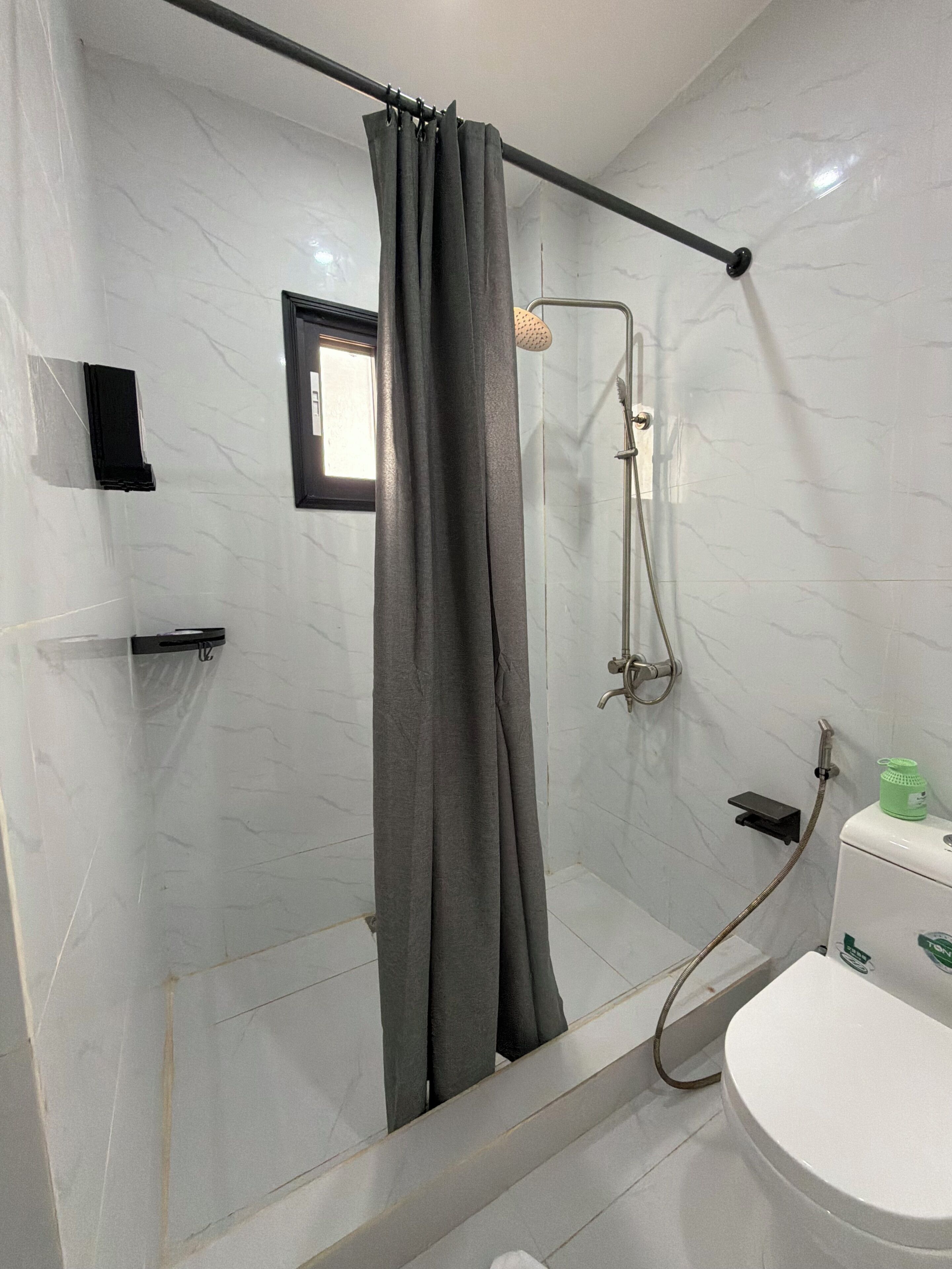 A bathroom with a shower, toilet, and a small shelf.