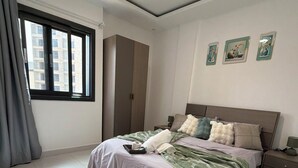 A bedroom with a bed, a wardrobe, a nightstand, a window with curtains, and three framed pictures on the wall. - 401: 2-bedroom apartment in perfect Dakar with cool AC, fast WiFi and comfort (Dakar)