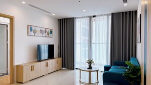 Uma sala de estar moderna com uma televisão de tela plana em um móvel de madeira, um sofá azul, uma mesa redonda pequena com um vaso e uma planta em vaso.
