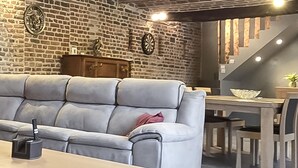 Een kamer met een grijze bank, een houten kast, een dartbord en een trap.