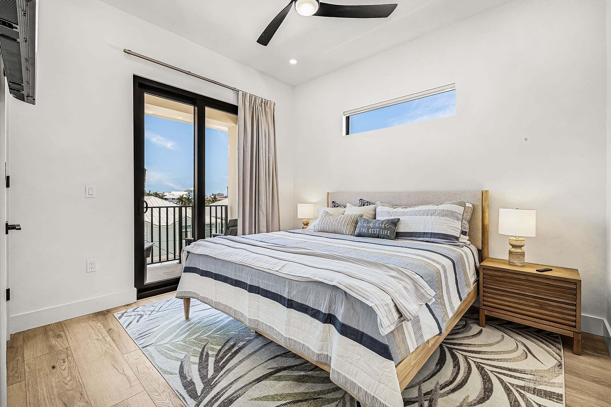 Une chambre à coucher comprenant un lit, des tables de chevet, un ventilateur de plafond, une fenêtre et une vue sur l’extérieur.