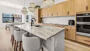 Una cucina moderna con isola in marmo, luci a sospensione, pensili in legno e un'ampia finestra.