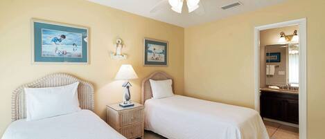 A hotel room with two beds, a ceiling fan, and artwork on the walls.