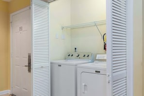 Een wasserette met twee Maytag wasmachines en drogers, een metalen plank en een deur met een bordje.