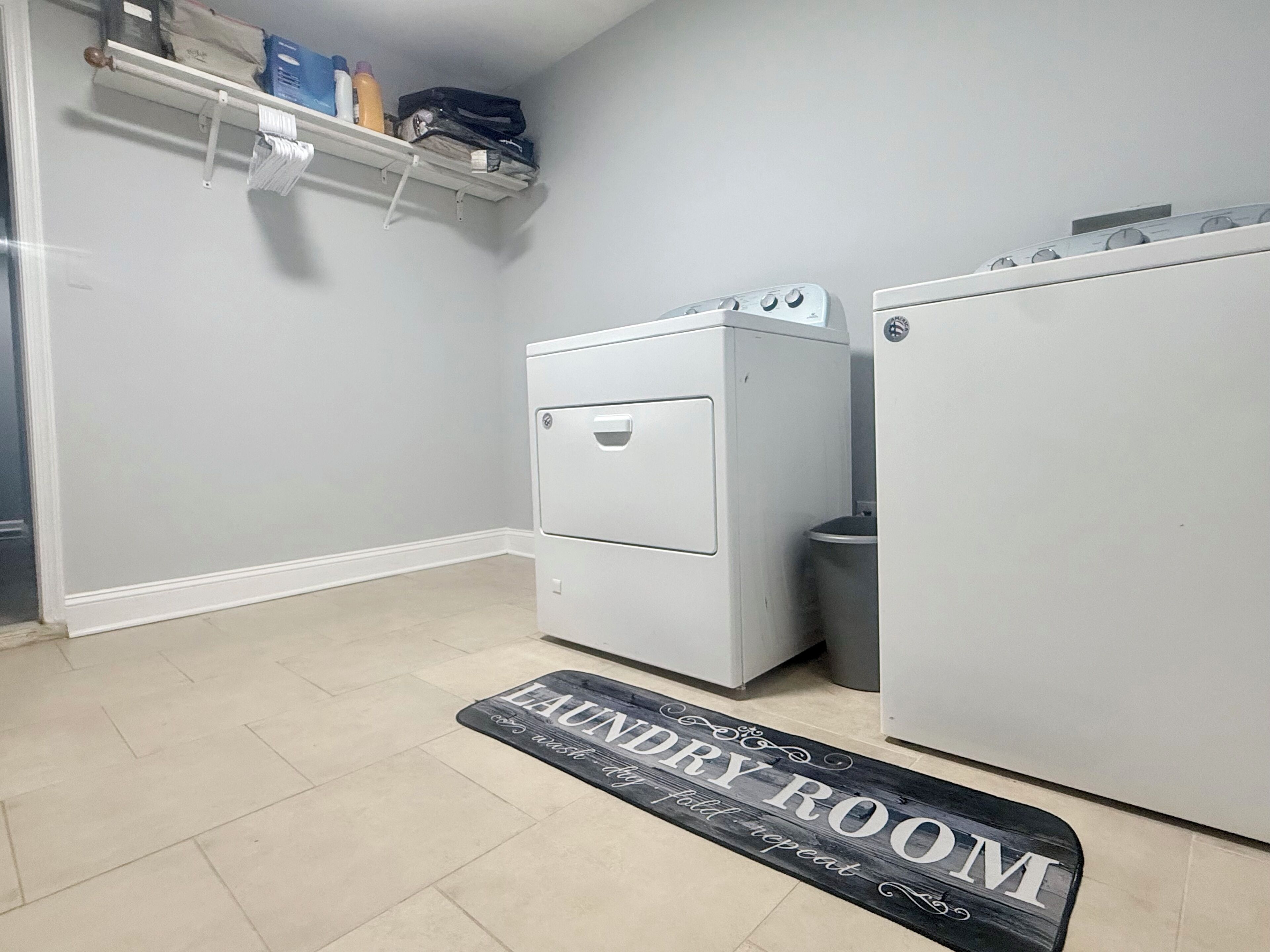 Une buanderie équipée d’un lave-linge, d’un sèche-linge et d’un paillasson sur lequel est écrit « BUANDERIE ».