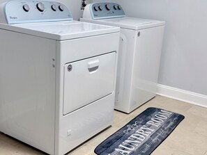 A laundry room with two white Whirlpool washers and dryers, a door handle, and a black mat with 'Laundry Room' written on it. - The NEW Happy Home, Warm & Perfect for Families (Springfield)