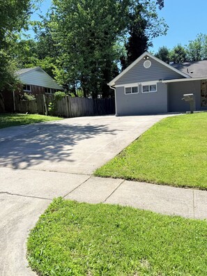A residential driveway leading to a house with a covered garage, surrounded by a wooden fence and lush greenery. - The NEW Happy Home, Warm & Perfect for Families (Springfield)