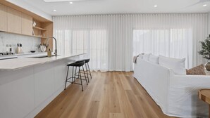 A modern kitchen with a central island, bar stools, and a dining area with a white sofa and curtains. - Woodlands Escape - 3 Bed, 2.5 Bath, Near Winery (Orange)