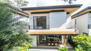 Una moderna casa a due piani con piscina, patio arredato e vegetazione lussureggiante.