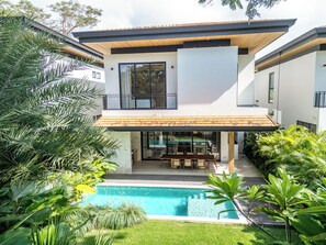 Ein modernes, zweistöckiges Haus mit Swimmingpool, einer Terrasse und Gartenmöbeln sowie üppiger Bepflanzung.