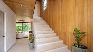 Una moderna scala con gradini bianchi, pareti in legno e vista su un soggiorno con un divano e piante.