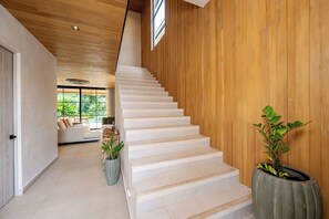 Eine moderne Treppe mit weißen Stufen, Holzwänden und Blick auf einen Wohnbereich mit einer Couch und Pflanzen.