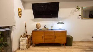 A living room with a wooden cabinet, a flat-screen TV, a mirror, and a small green ottoman. - Modern Townhouse in the Heart of Mixcoac! (Ciudad de México)