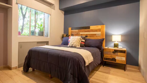 A bedroom with a bed, a nightstand, a window, and a wall with a dark blue accent. - Modern Townhouse in the Heart of Mixcoac! (Ciudad de México)